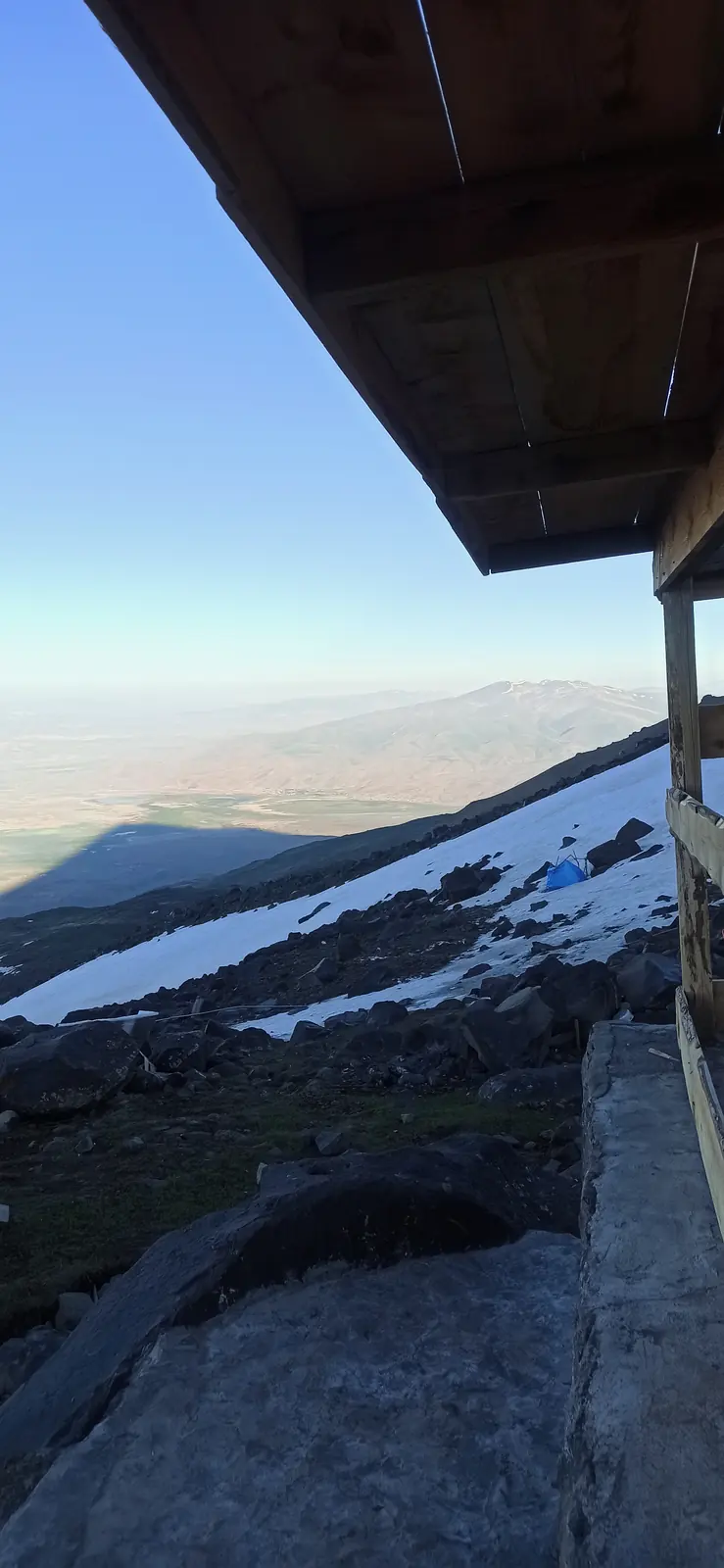The edge of a wooden hut roof above snowy slopes, early morning