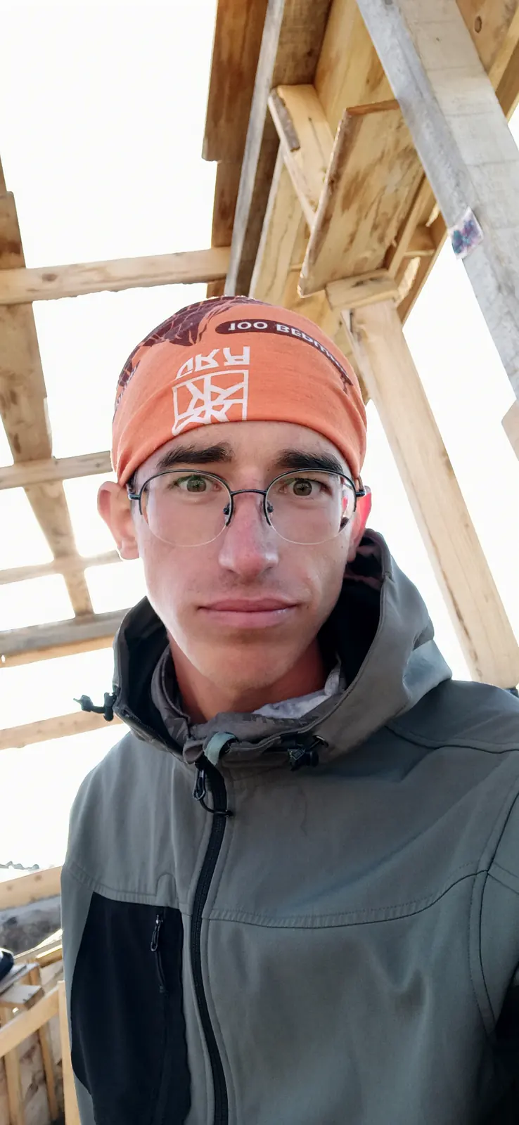 Andrii in an orange headband and a grey jacket by a wooden hut