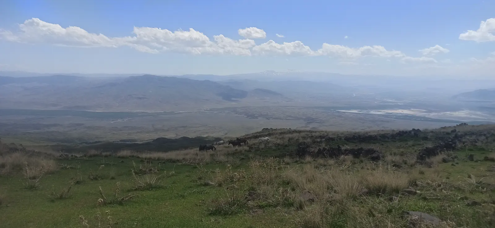 A wide plain far below, seen from grassy slopes under clouds
