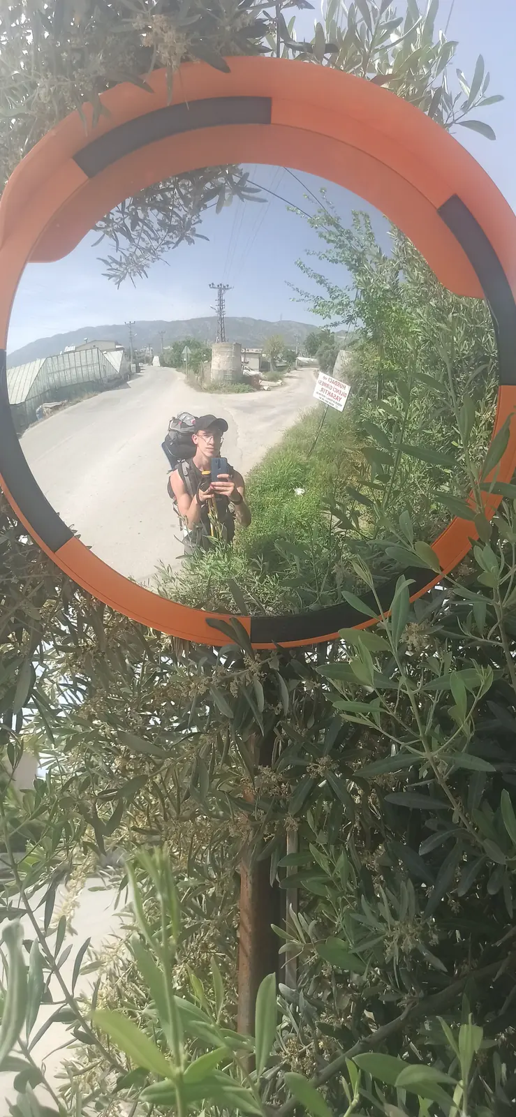 Andrii reflected in a round orange-framed road mirror among bushes