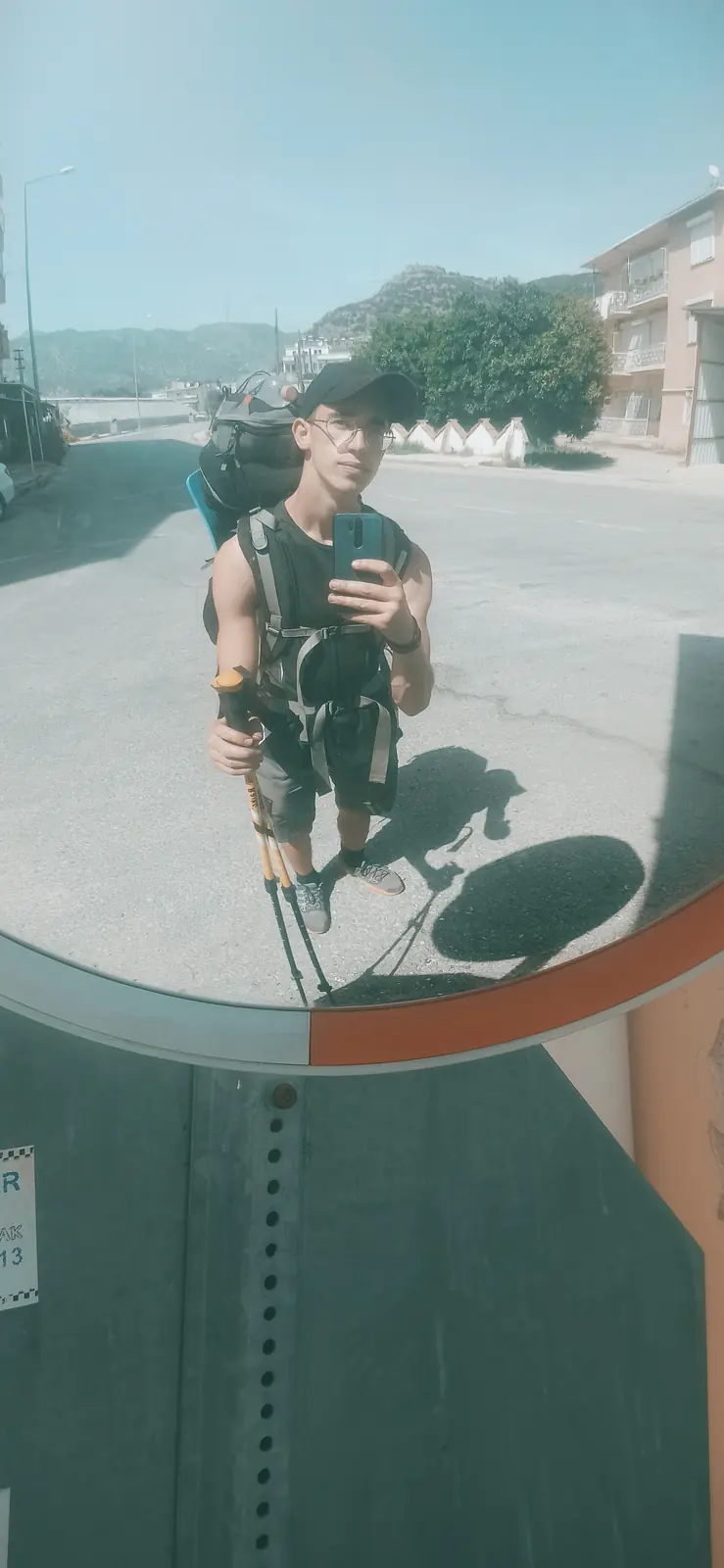 Another road-mirror reflection of Andrii with his backpack on a sunny street