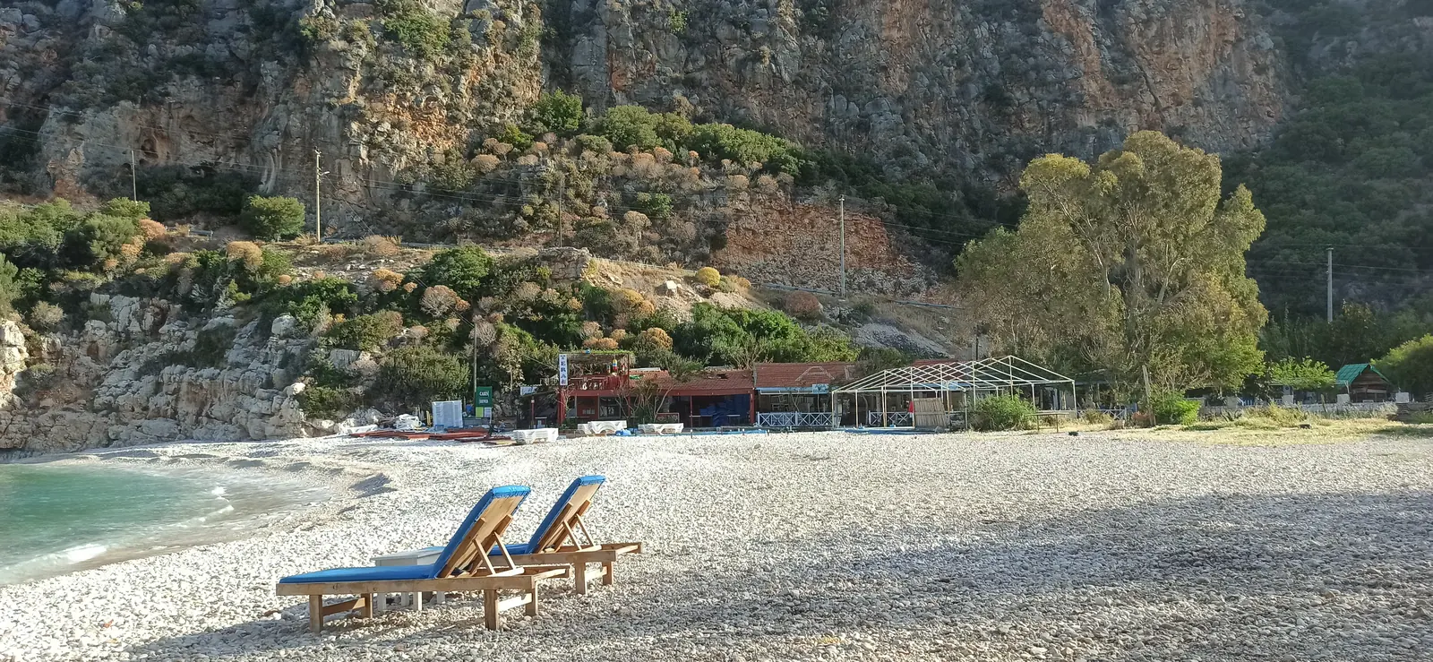Two sunbeds on a pebble beach below tall orange cliffs