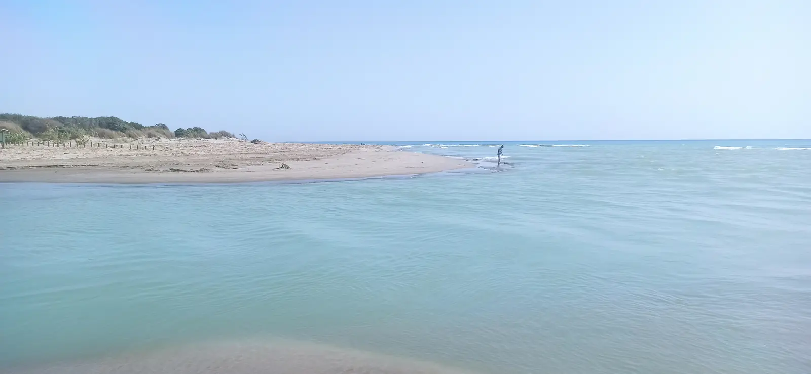 A wide turquoise river mouth meeting the sea, with dunes on the far bank