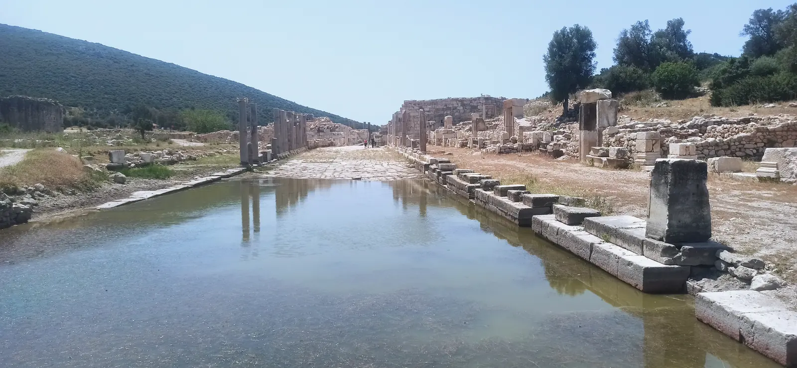 A flooded ancient colonnaded street lined with column bases