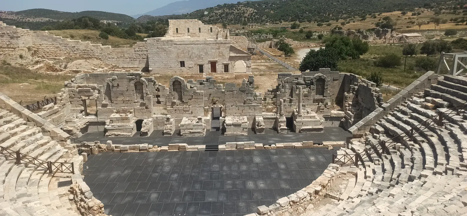The stone seats of an ancient theatre with a ruined building behind