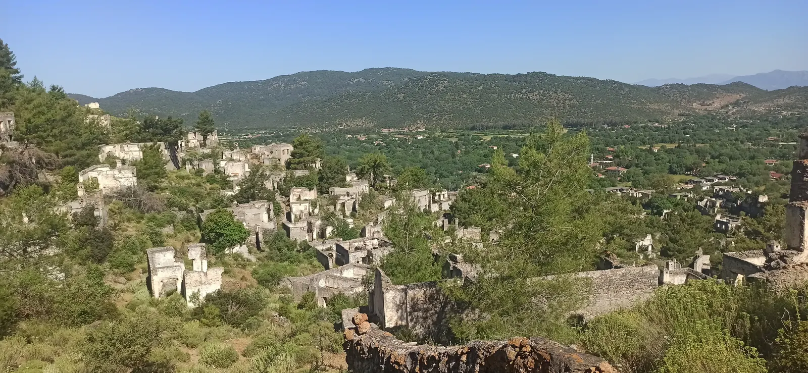 Roofless stone houses of an abandoned village spread over a green hillside