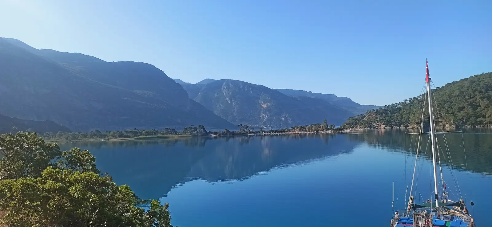 Still blue water reflecting mountains, with a sailing boat