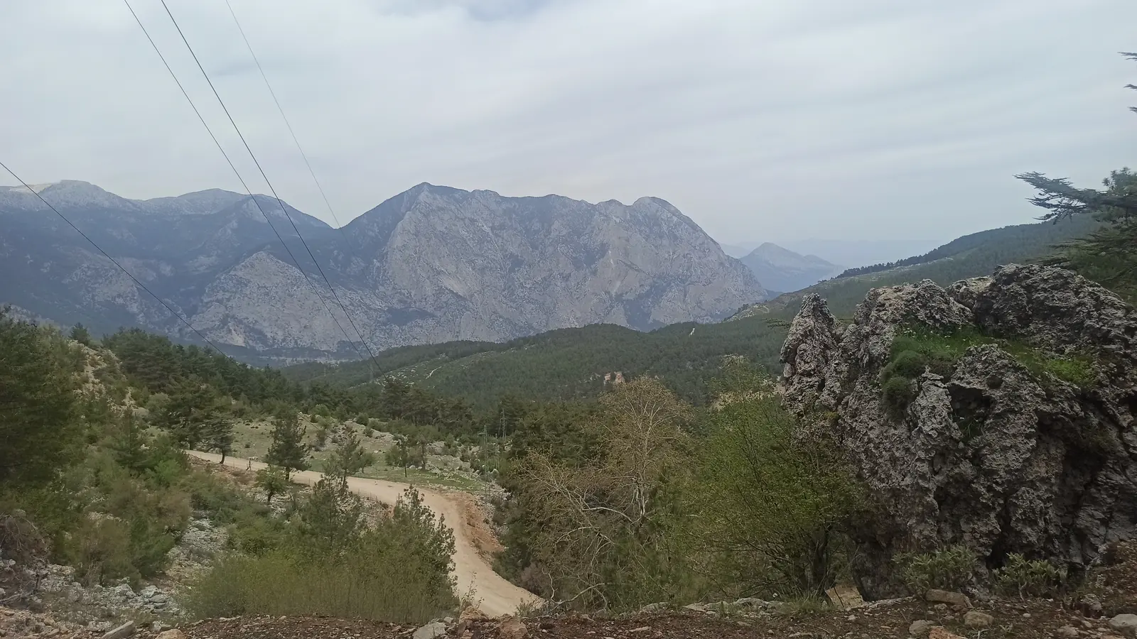 A dirt road winding down a valley towards grey limestone mountains under cloud