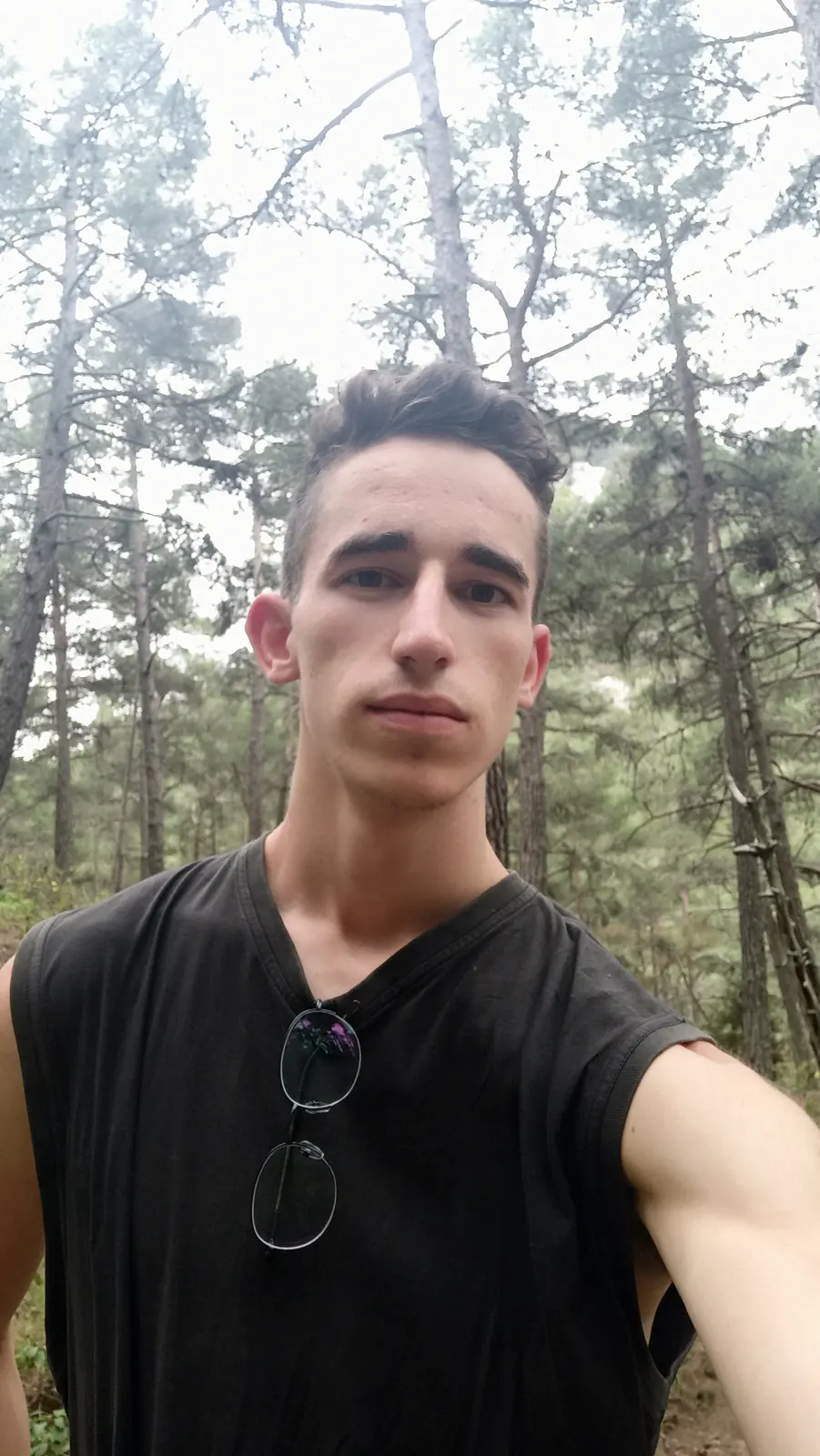 Andrii in a sleeveless black T-shirt with sunglasses hooked on it, in a pine forest