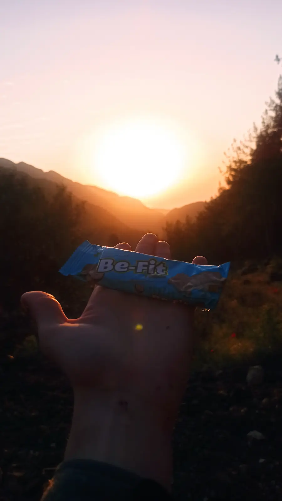 A hand holding a snack bar up to the low sun