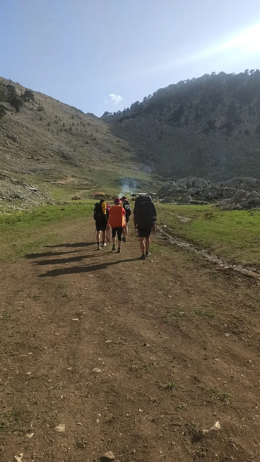 Three hikers walking across a meadow towards tents below rocks