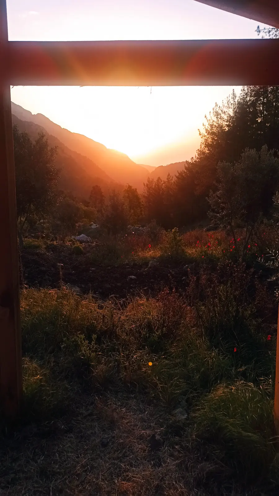 Sunrise between two dark mountain slopes, framed by a wooden beam