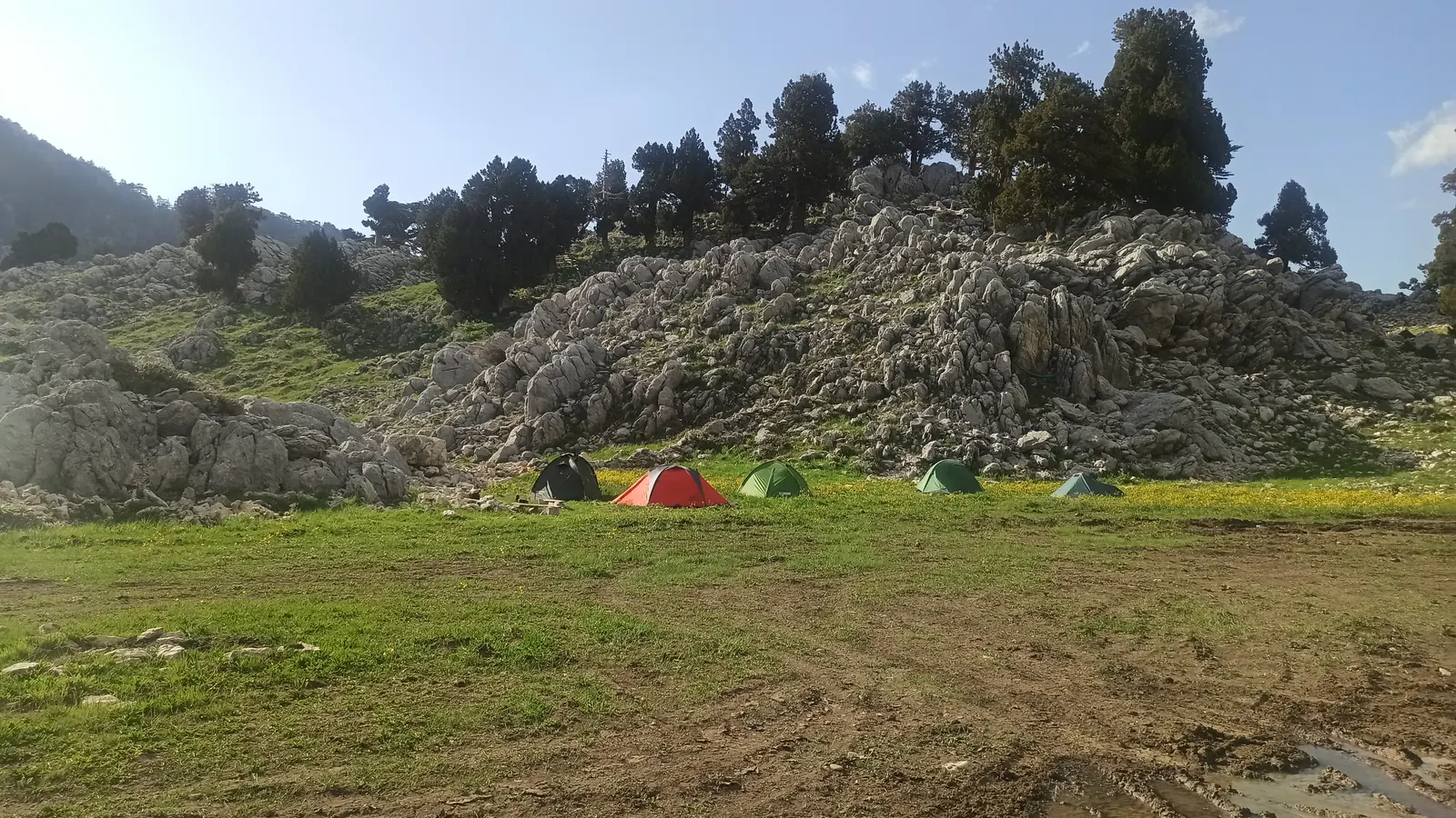 Colourful tents on a green meadow below a ridge of grey limestone