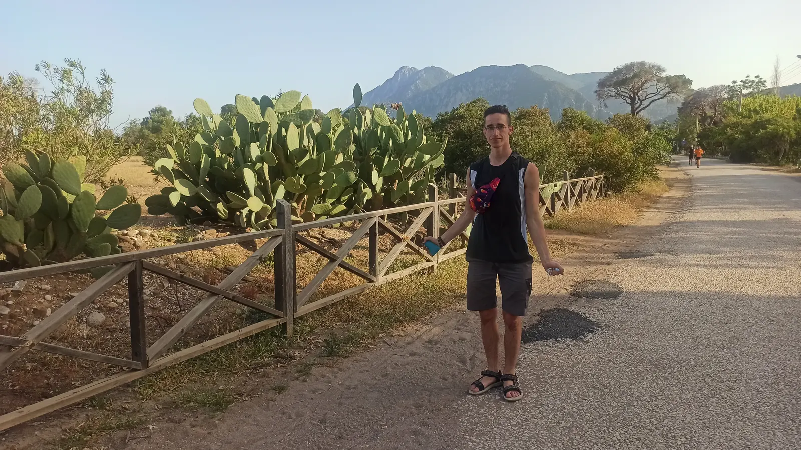 Andrii on a road lined with prickly pear cactus and a wooden fence