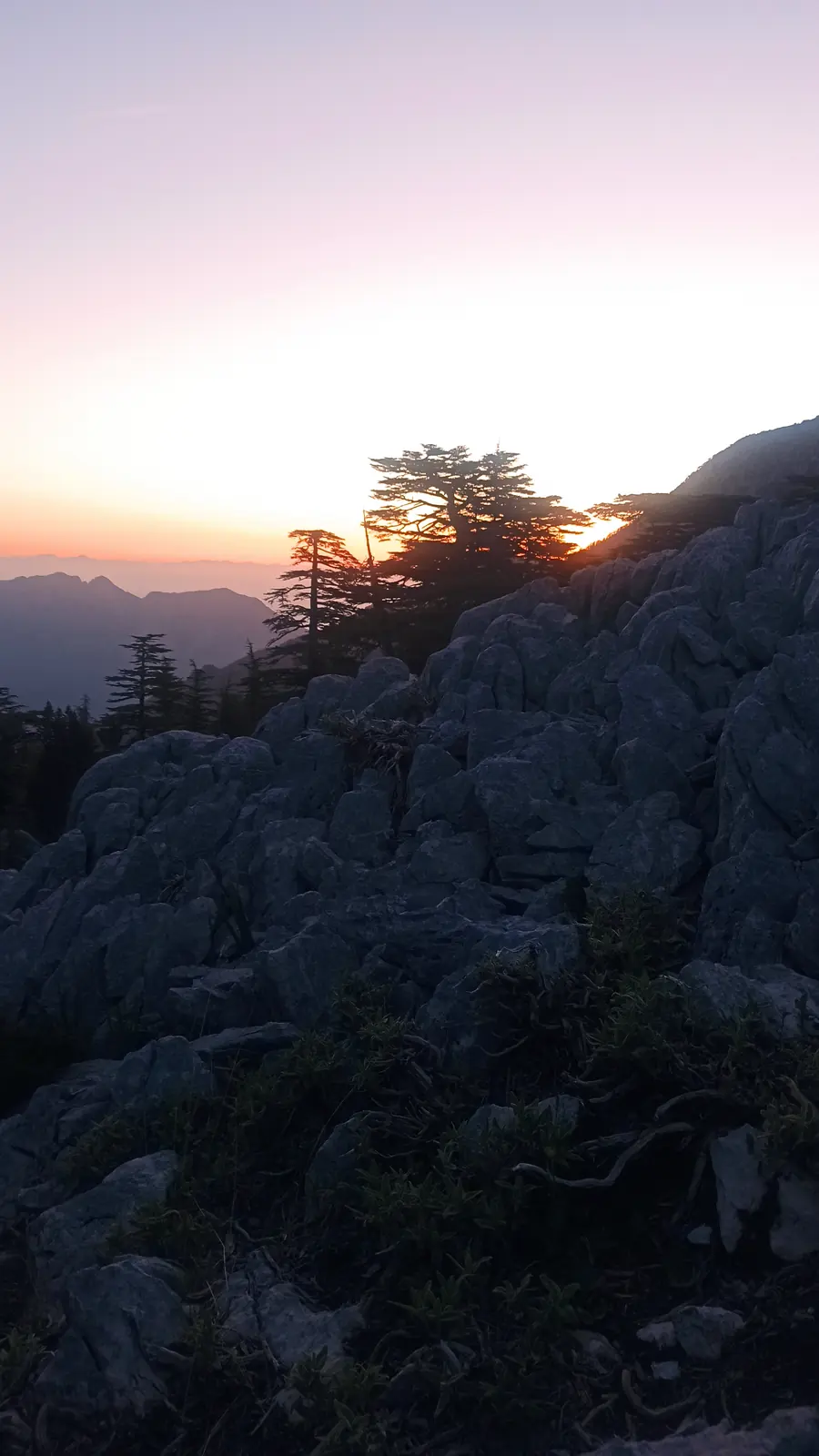 Pink dawn sky over a dark rocky slope