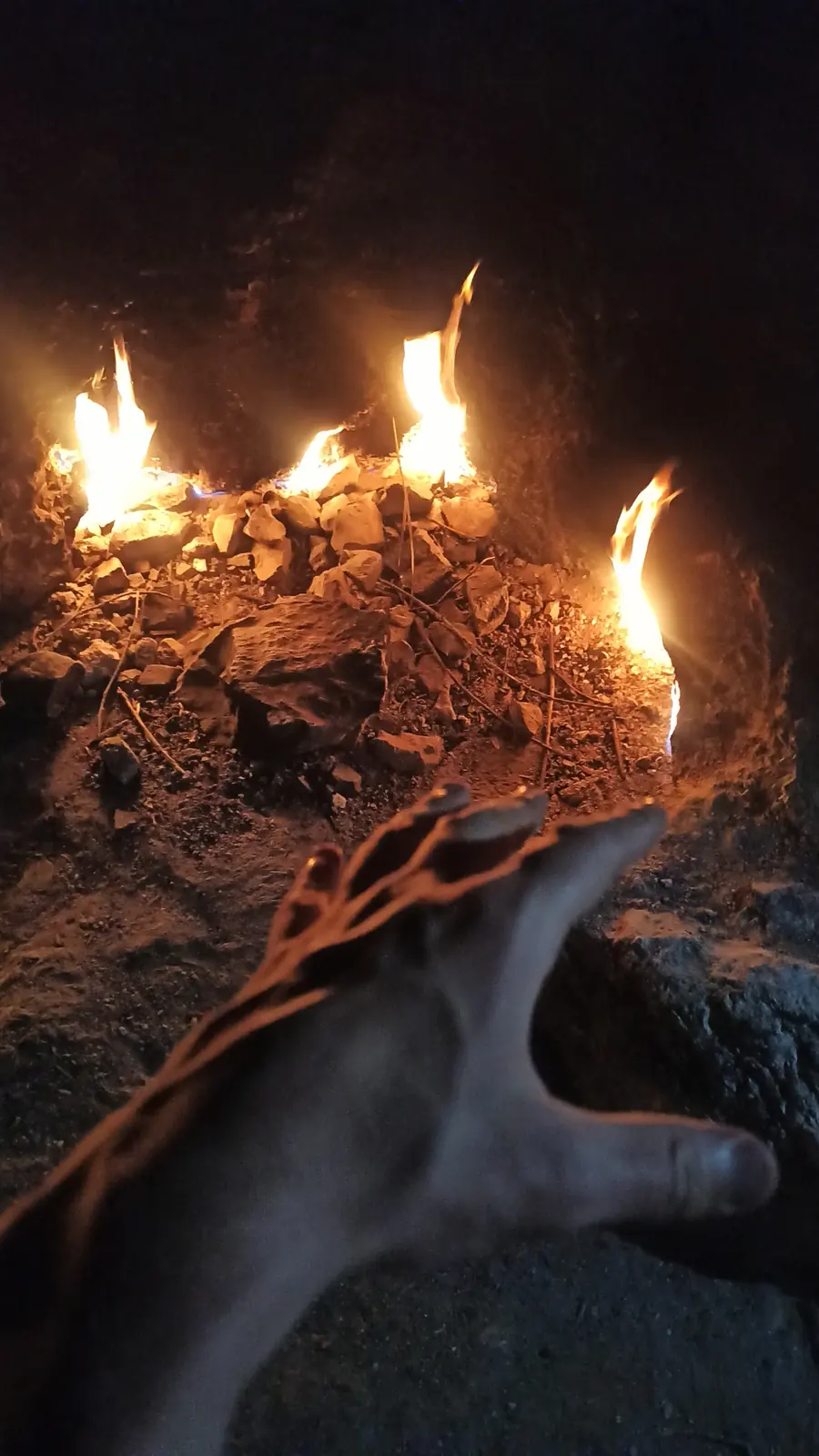 Small flames burning out of cracks in a rock at night, a hand held near them