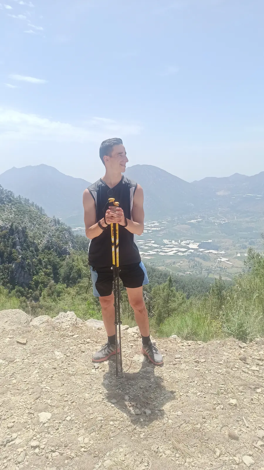 Andrii with trekking poles on a hilltop above a coastal valley