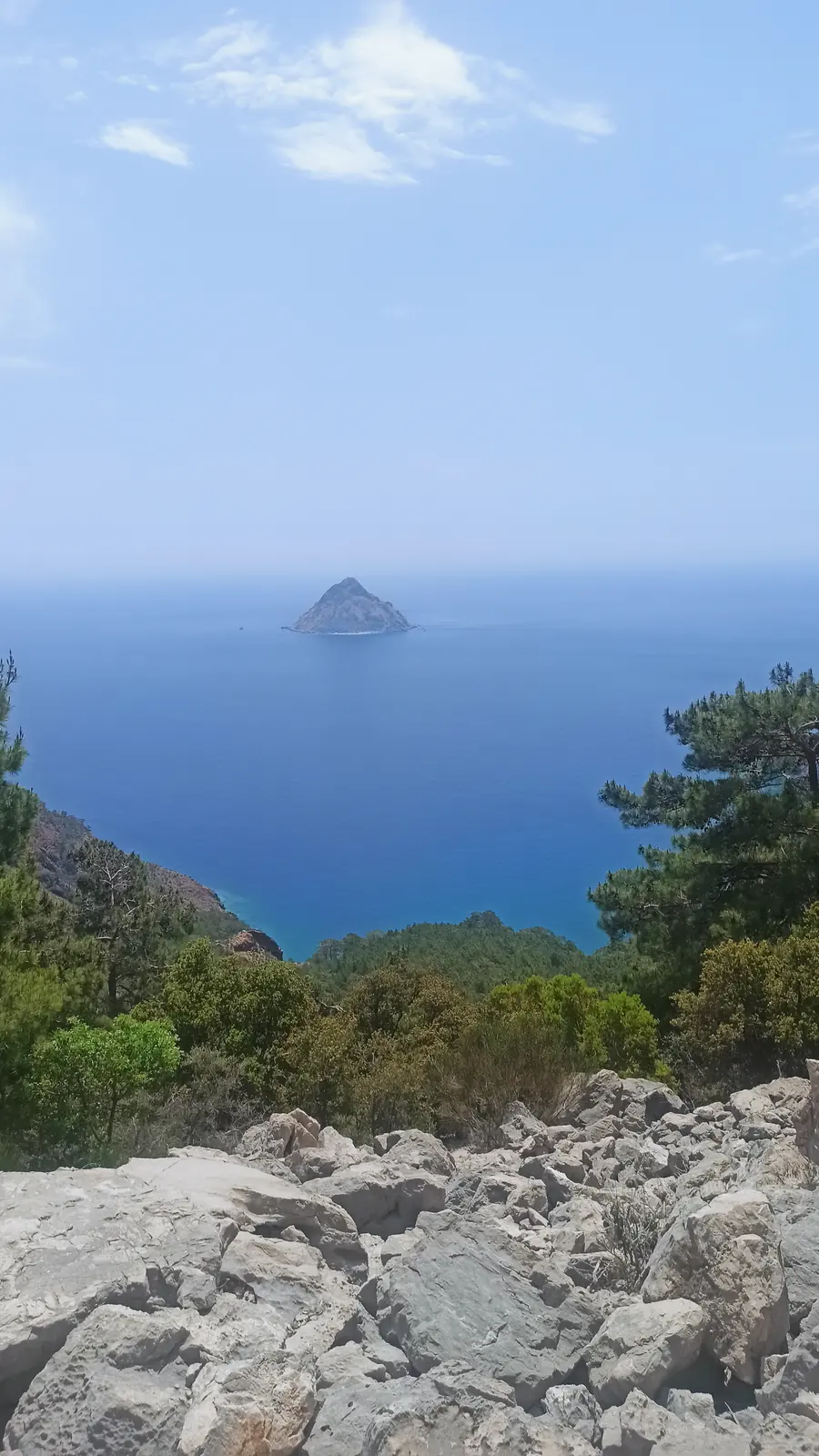 A small rocky island in a deep blue sea, seen from a rocky slope