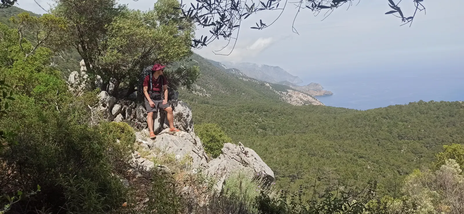 A hiker resting on a rock above a wooded coast