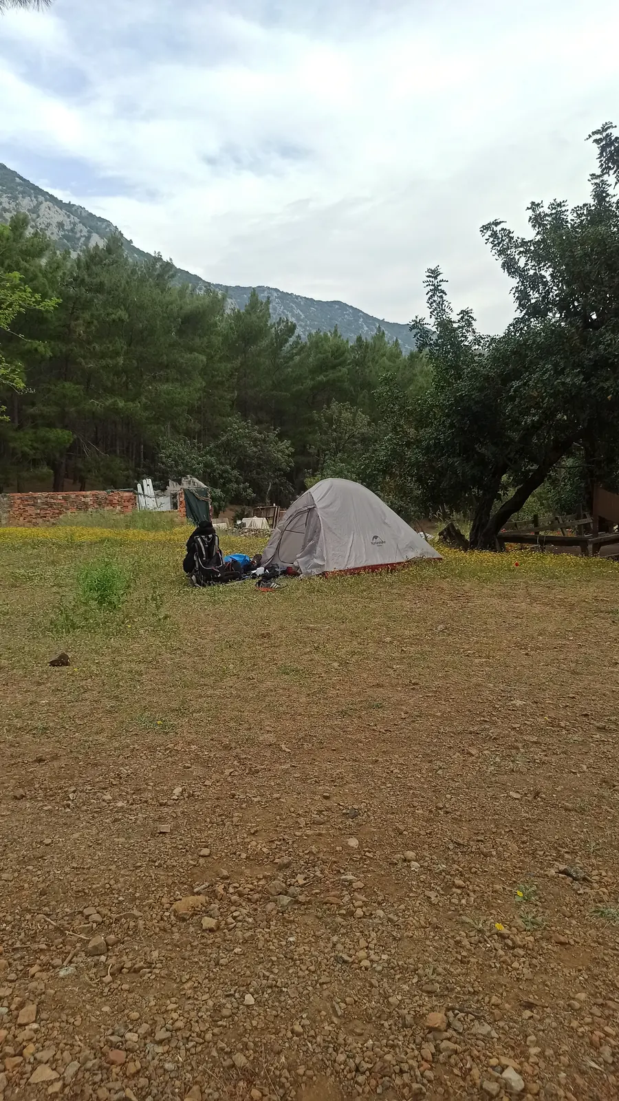 A small tent on a grassy field below wooded hills