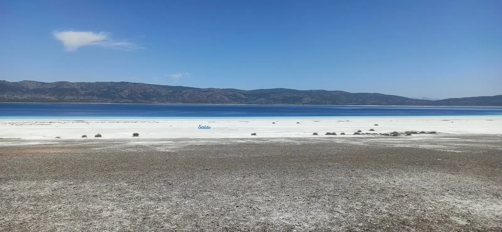 A bright white shore and a deep blue lake under a clear sky
