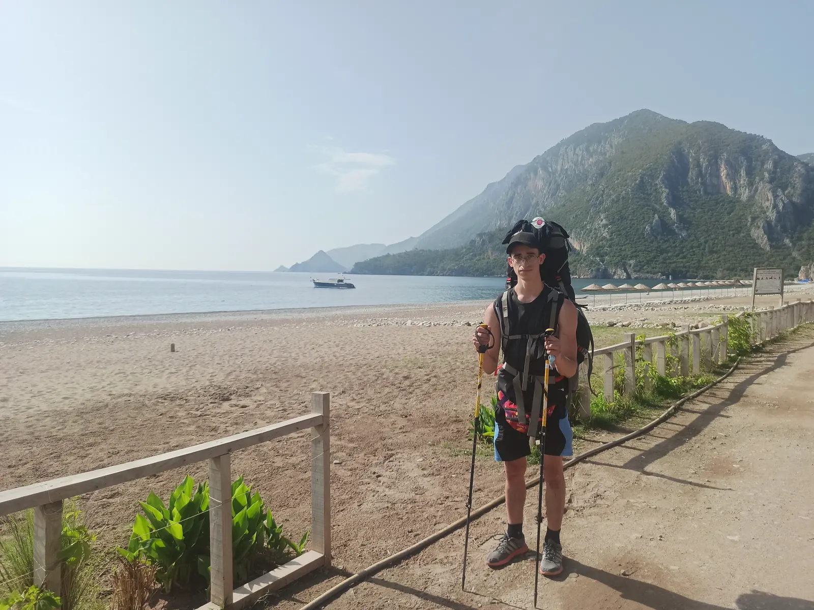 Andrii with a large backpack and trekking poles on a beach below a steep green mountain