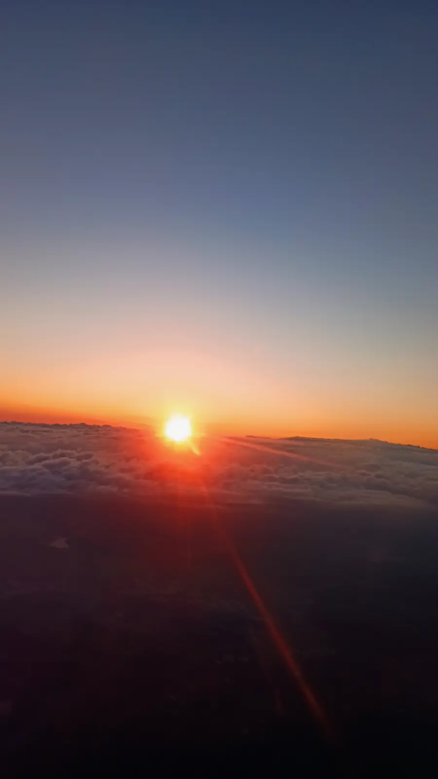 The sun rising over a dark layer of cloud, seen from a plane window